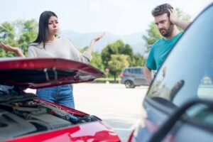 A man and woman standing next to a car with the hood open, discussing a car accident issue.