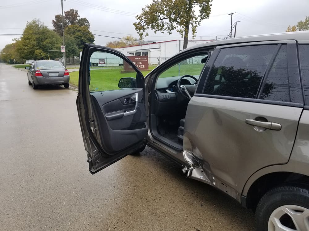 tan colored SUV with driver side door open and dent in rear passenger side of body