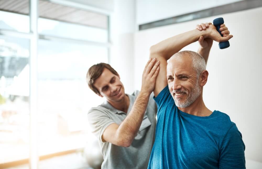 physiotherapist and mature man with dumbbell in clinic for physical therapy